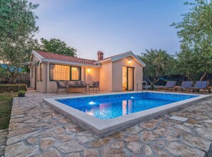 Une maison avec une piscine, une terrasse en pierre et du mobilier d’extérieur.