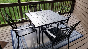 Terraza de madera con una mesa y sillas, rodeada por una barandilla y follaje.