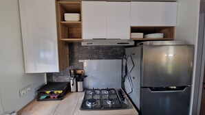 Una cocina compacta con estufa a gas, refrigerador de acero inoxidable y alacenas de madera.