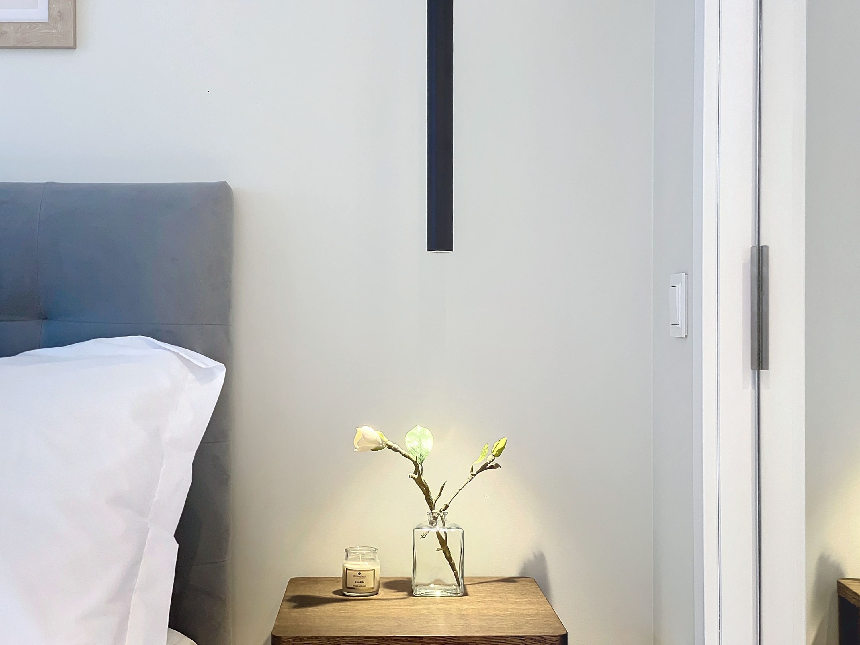 A bedroom with a bed, a bedside table with a vase and candle, and a door.