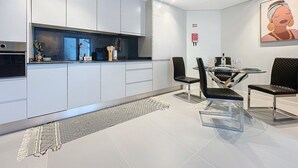 Una cucina moderna con mobili bianchi, un'area pranzo con tavolo in vetro e sedie nere, e un grande quadro astratto appeso alla parete.