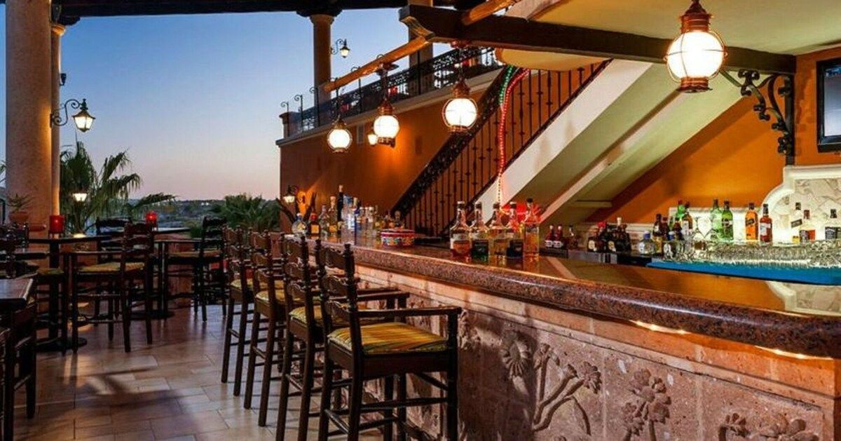 A bar area with a counter, chairs, and bottles.