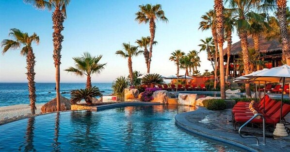 A pool area with palm trees, lounge chairs, and a view of the ocean.