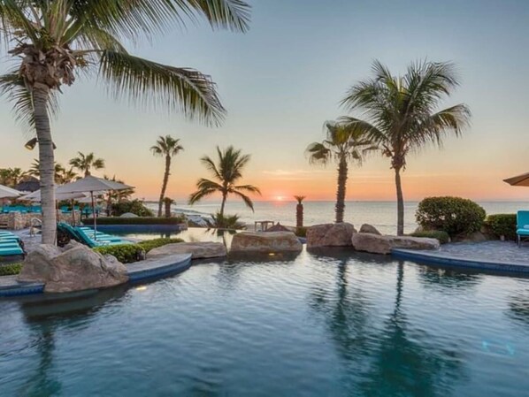 A pool area with lounge chairs and palm trees, overlooking a body of water.