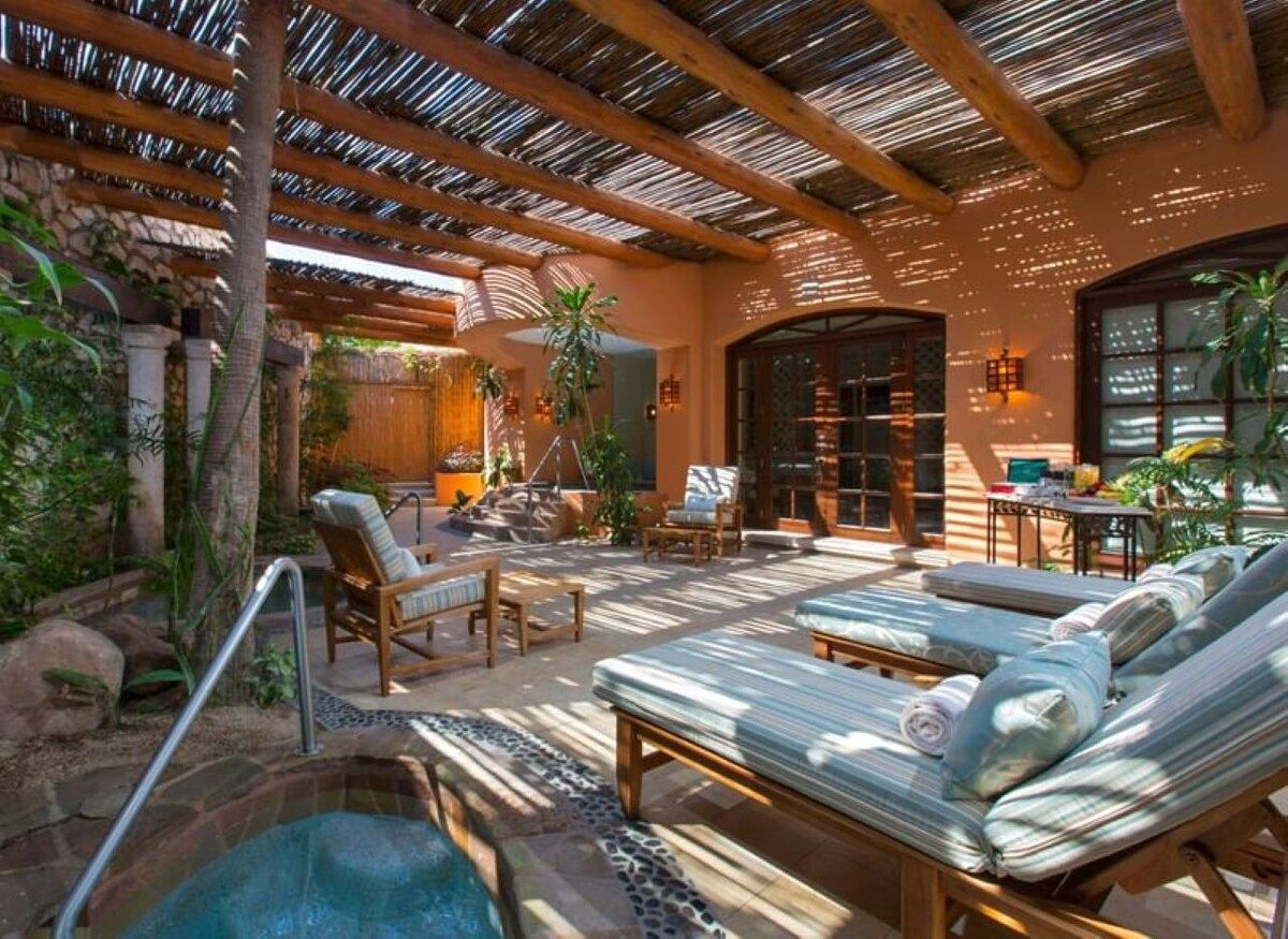 A pool area with lounge chairs, a hot tub, and a covered patio with wooden beams.