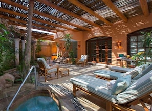 A pool area with lounge chairs, a hot tub, and a covered patio with wooden beams.