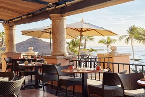An outdoor seating area with tables and chairs, umbrellas, and a view of the ocean.