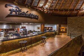 A restaurant with a counter, stools, and a thatched roof ceiling.