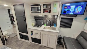 A compact kitchenette with a microwave, stove, sink, and a flat-screen TV displaying streaming services. - Come Glamping in this luxurious 2022 RV in DT FT MYERS, Very Private Space! (Fort Myers)