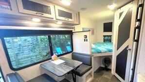 A compact RV interior with a dining area, a small kitchenette, and a sleeping berth. - Come Glamping in this luxurious 2022 RV in DT FT MYERS, Very Private Space! (Fort Myers)