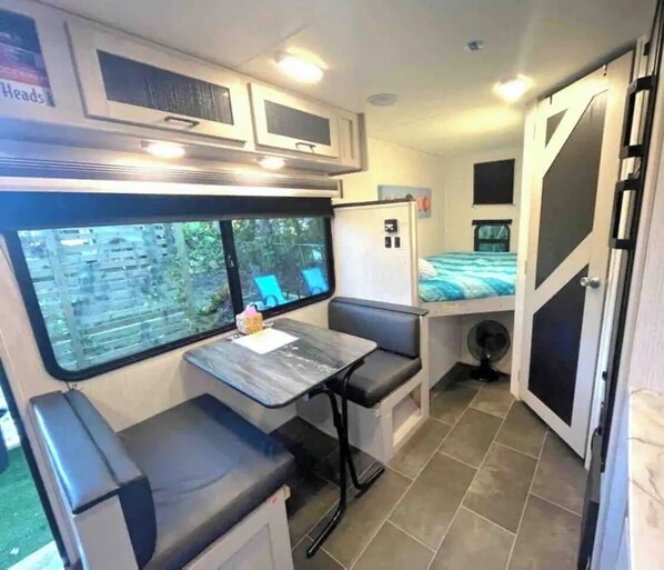 A compact RV interior with a dining area, a small kitchenette, and a sleeping berth.