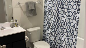 Une salle de bain avec des toilettes blanches, un meuble-lavabo noir, un lavabo blanc et un rideau de douche à motifs géométriques.