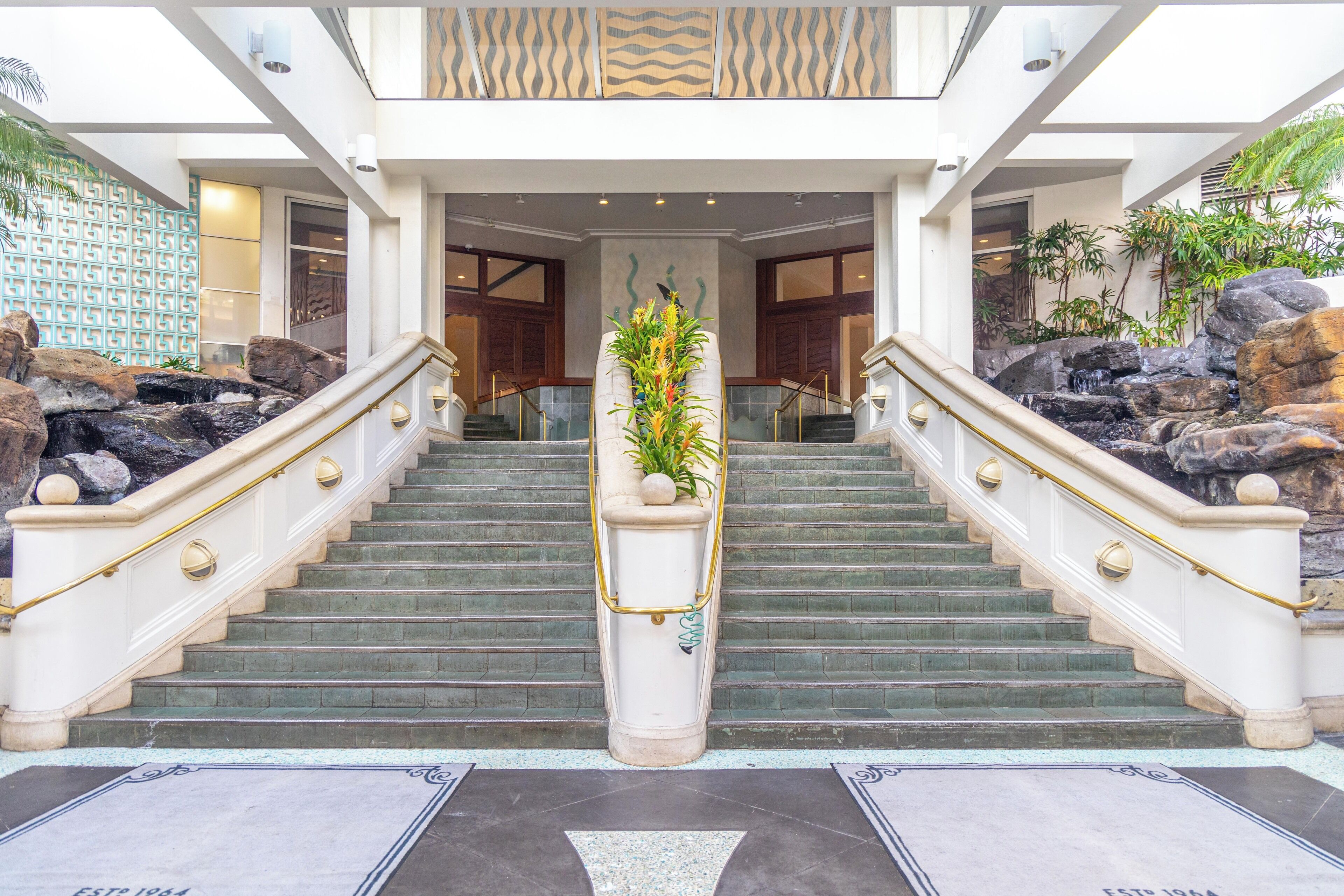 A grand staircase with a central planter, flanked by large rocks and leading to a building entrance.
