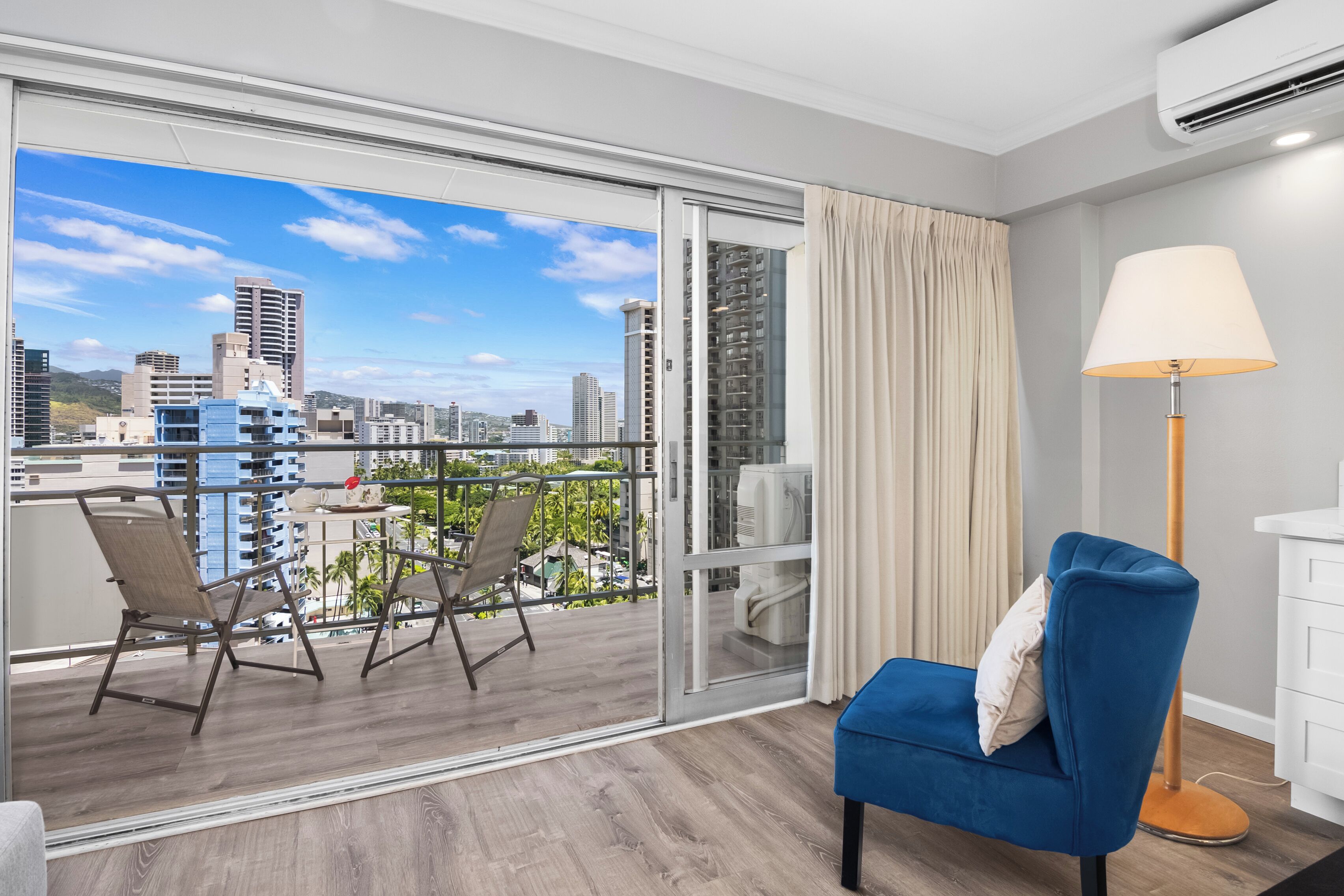 A modern hotel room with a balcony, a blue chair, a table, and a lamp.