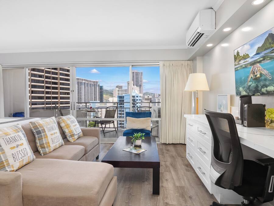 Quarto de hotel moderno com sofá, escrivaninha e uma grande janela com vista para a cidade.