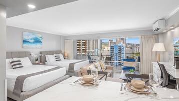 A modern hotel room with two beds, a dining area, and a balcony with a city view.