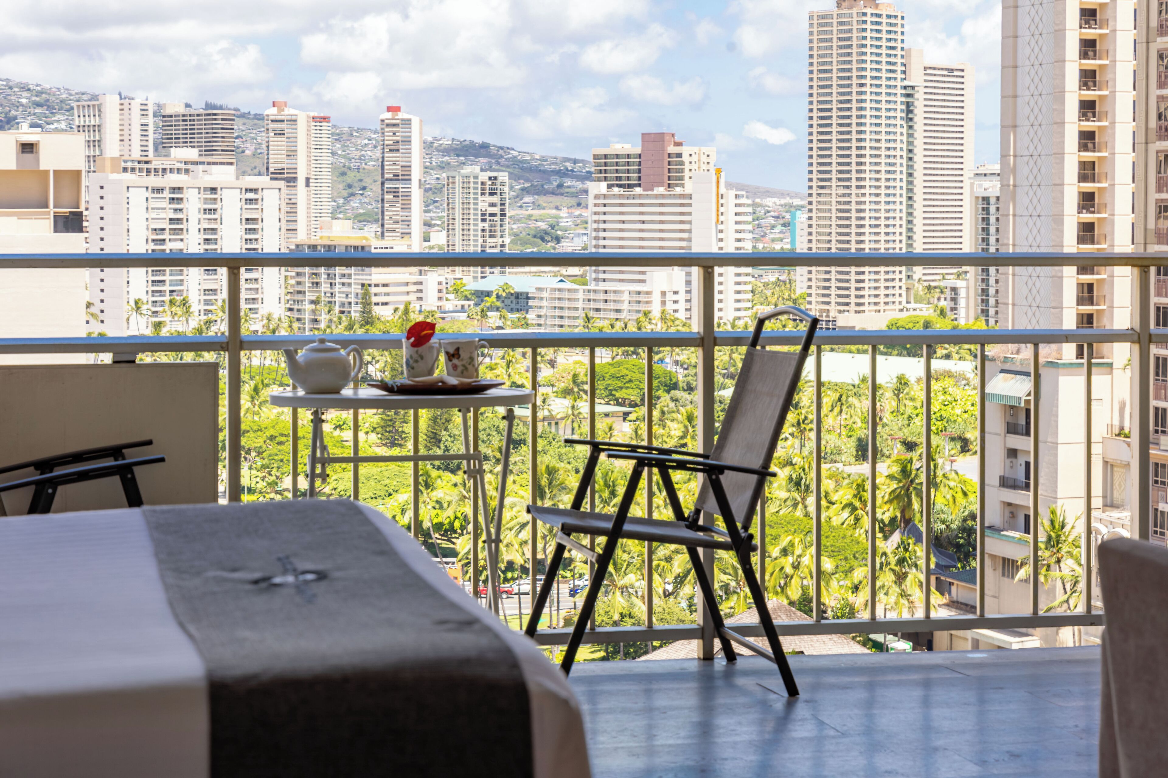 Un balcon avec un lit, une chaise et une petite table sur laquelle se trouvent une théière et une tasse.