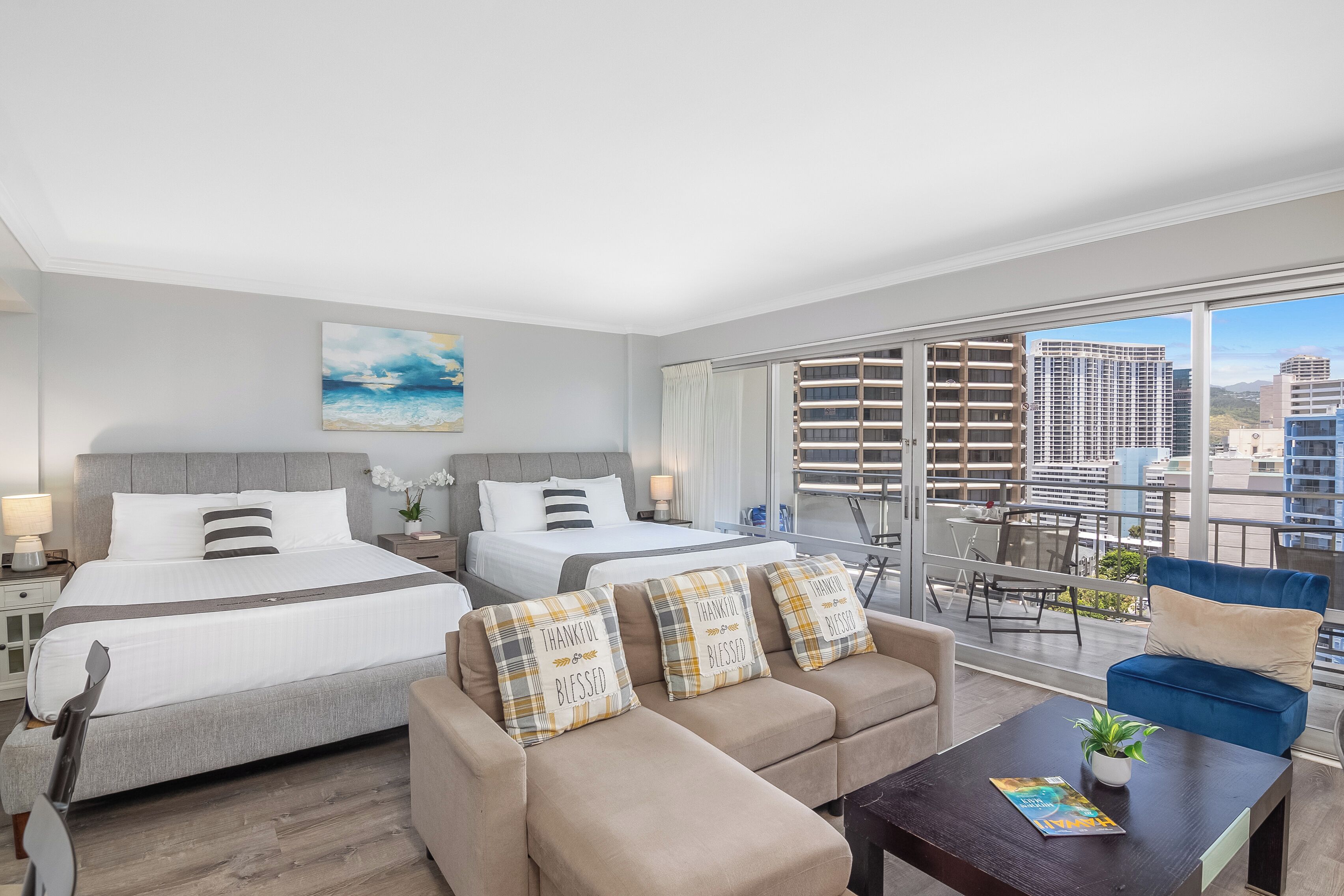 A modern hotel room with two beds, a balcony with a city view, and a seating area with a coffee table.