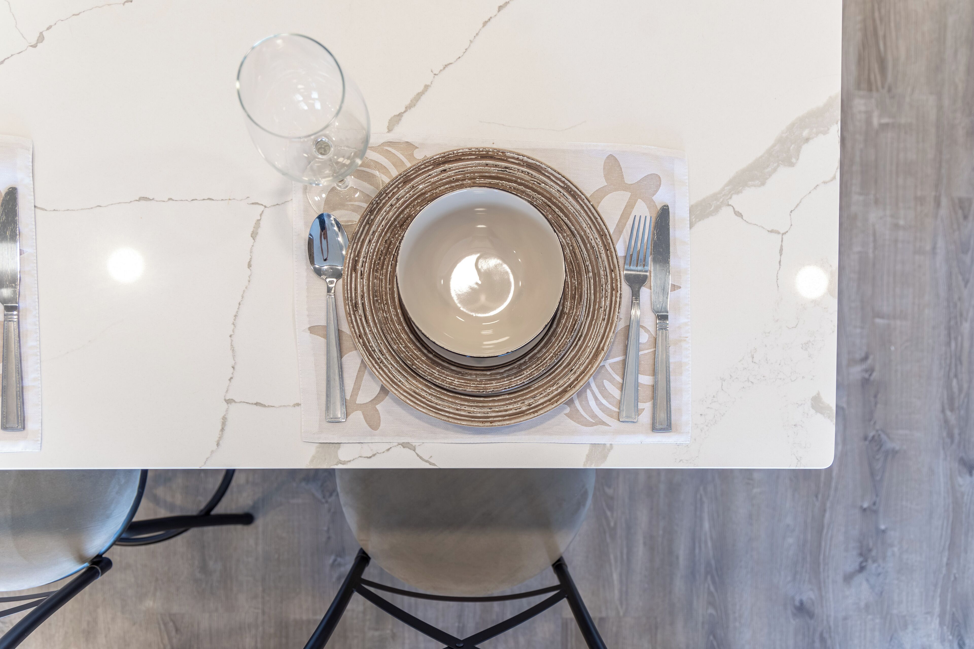 Una mesa dispuesta con cubierta de mármol blanco, un plato con borde dorado y una copa de vidrio transparente.