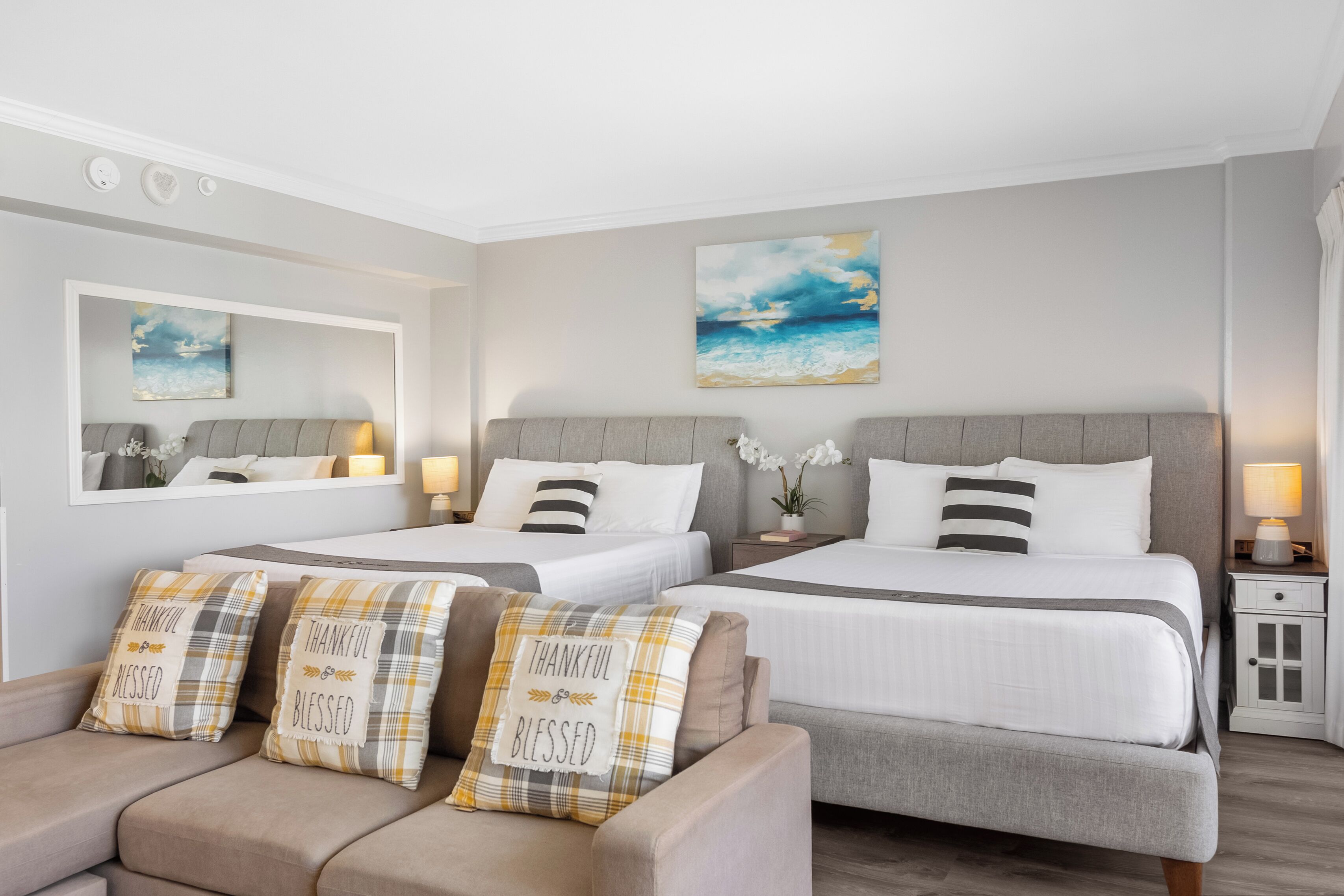 Een hotelkamer met twee bedden, een bank, een spiegel en kunstwerken aan de wanden.