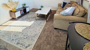 Una sala de estar con una televisión de pantalla plana, un sofá, una mesa de centro y una pared decorada con cestas tejidas y pinturas.