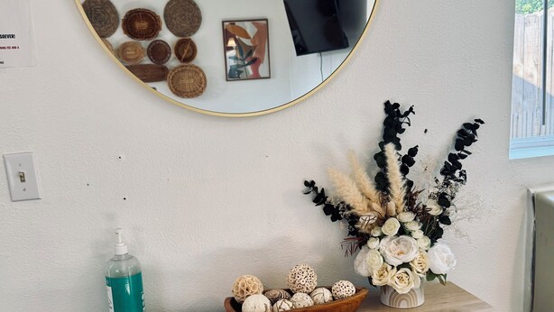 Una consola de madera con un espejo, un cuenco de objetos decorativos, un dispensador de gel antibacterial y un documento.