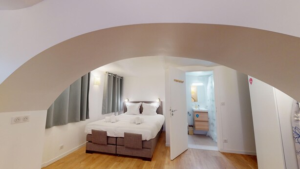 A bedroom with a bed, a bathroom, and a view through an arched doorway. - Studio Castelnau (Strasbourg)