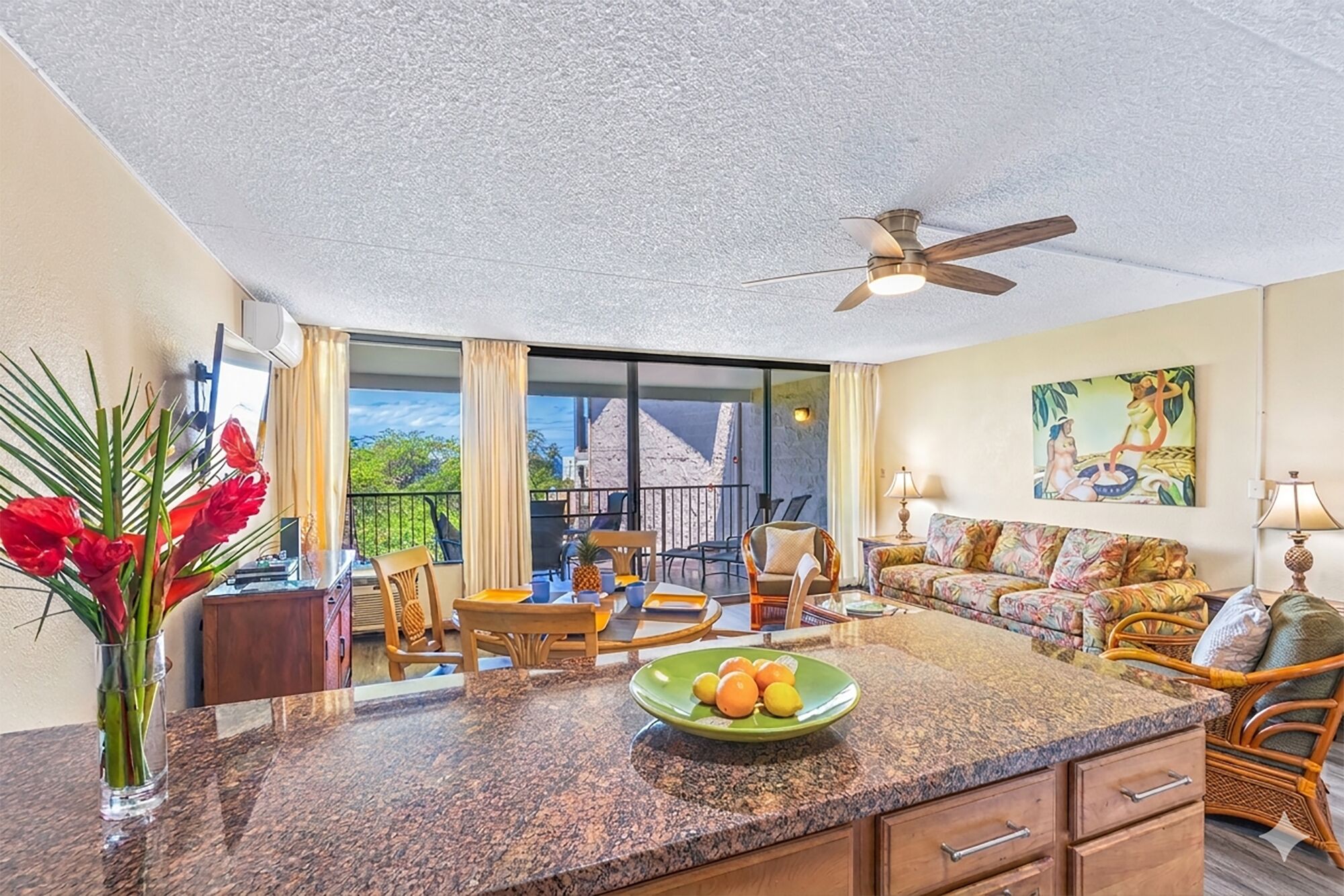 A spacious living area with a kitchen counter, dining table, and chairs, a ceiling fan, and a large window with a view.