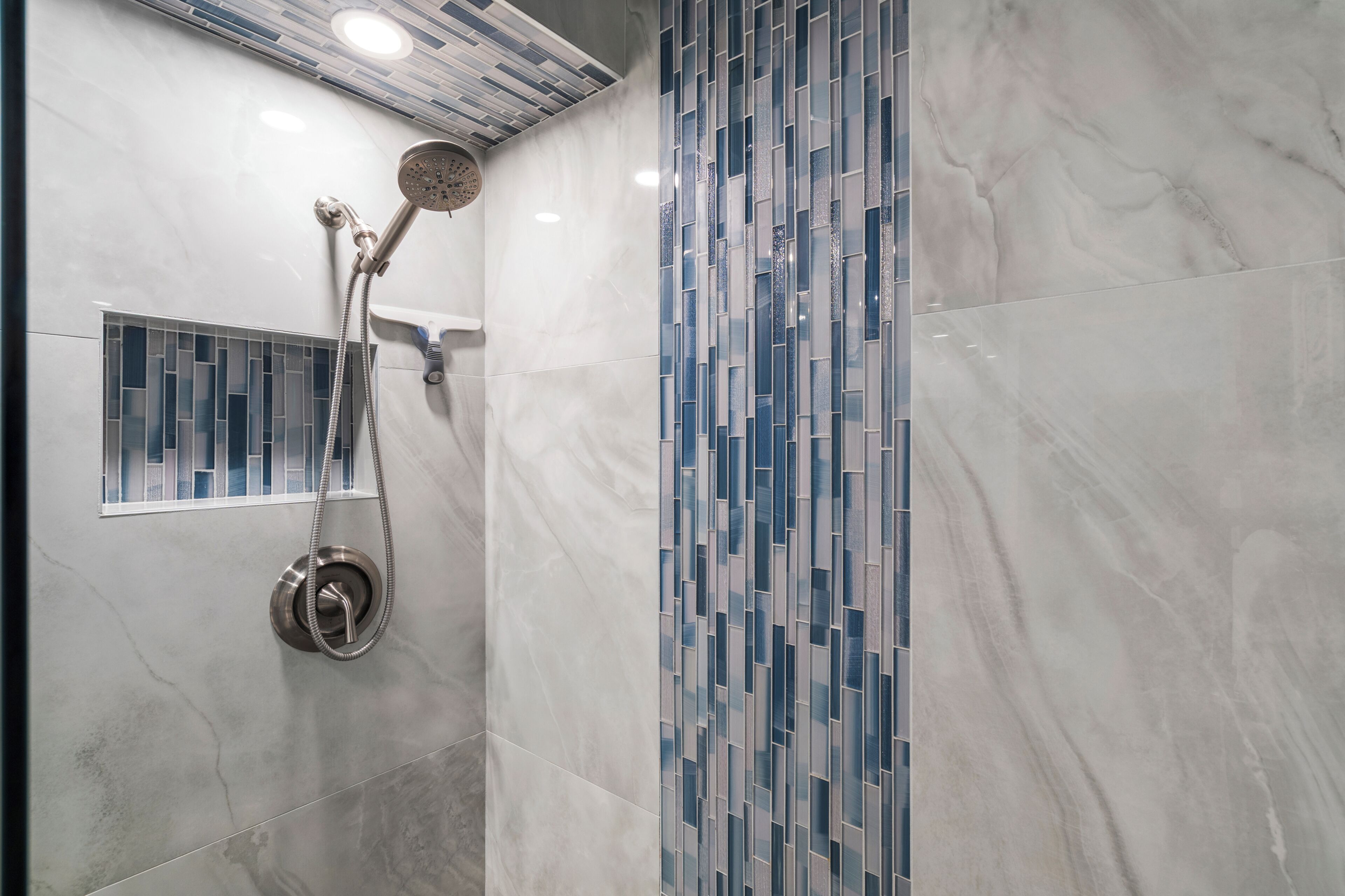 A bathroom with a shower, a tiled wall, and a vent.