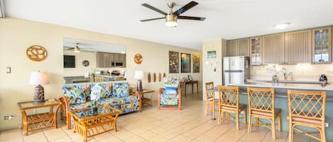 A living room with a sofa, chairs, a dining area with a table, and a kitchen with cabinets and a refrigerator.