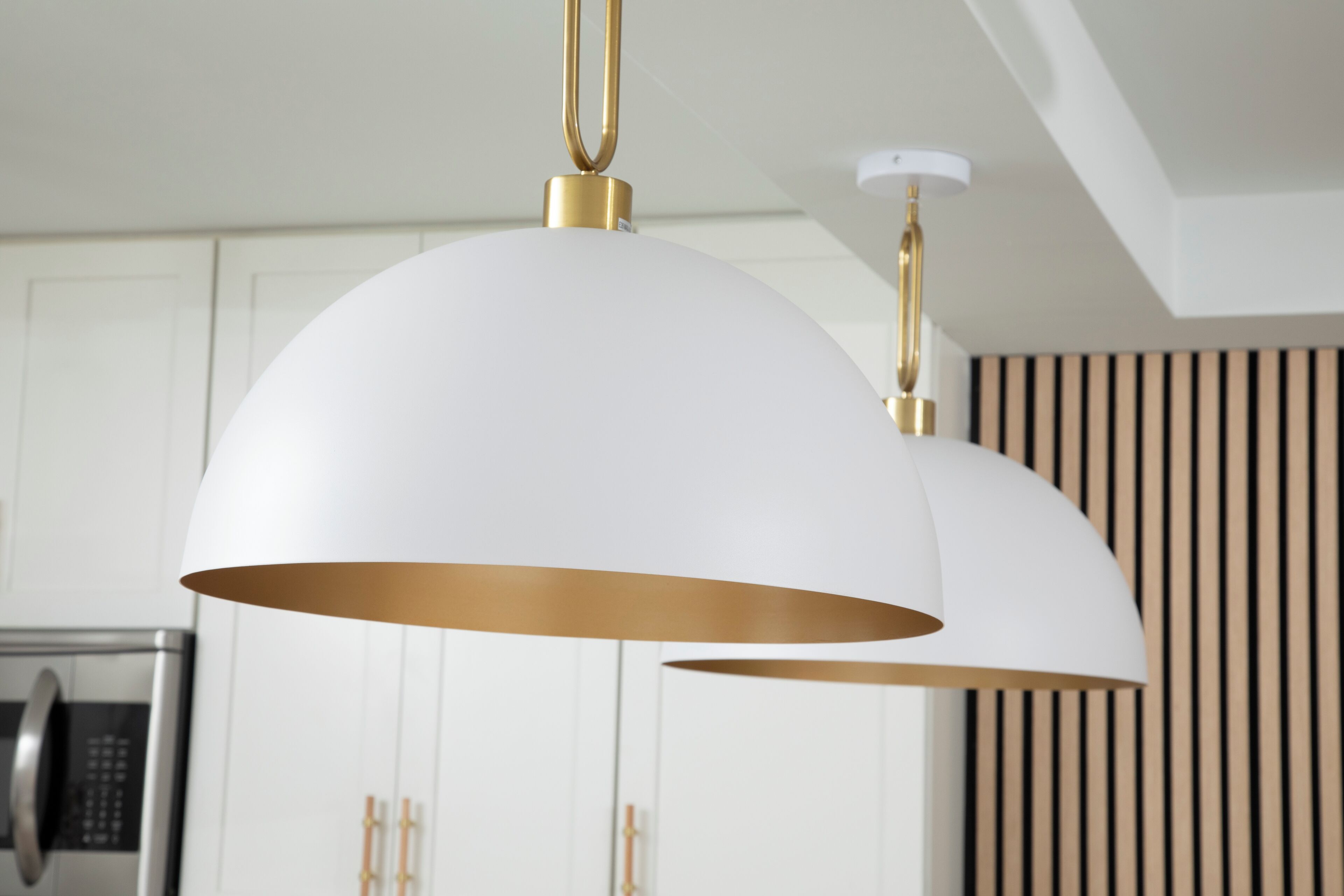 Cozinha moderna com armários brancos, forno de aço inoxidável e luminária pendente com base dourada.
