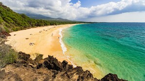 Une plage à l’eau turquoise et limpide, bordée d’un rivage sablonneux et ponctuée de formations rocheuses.