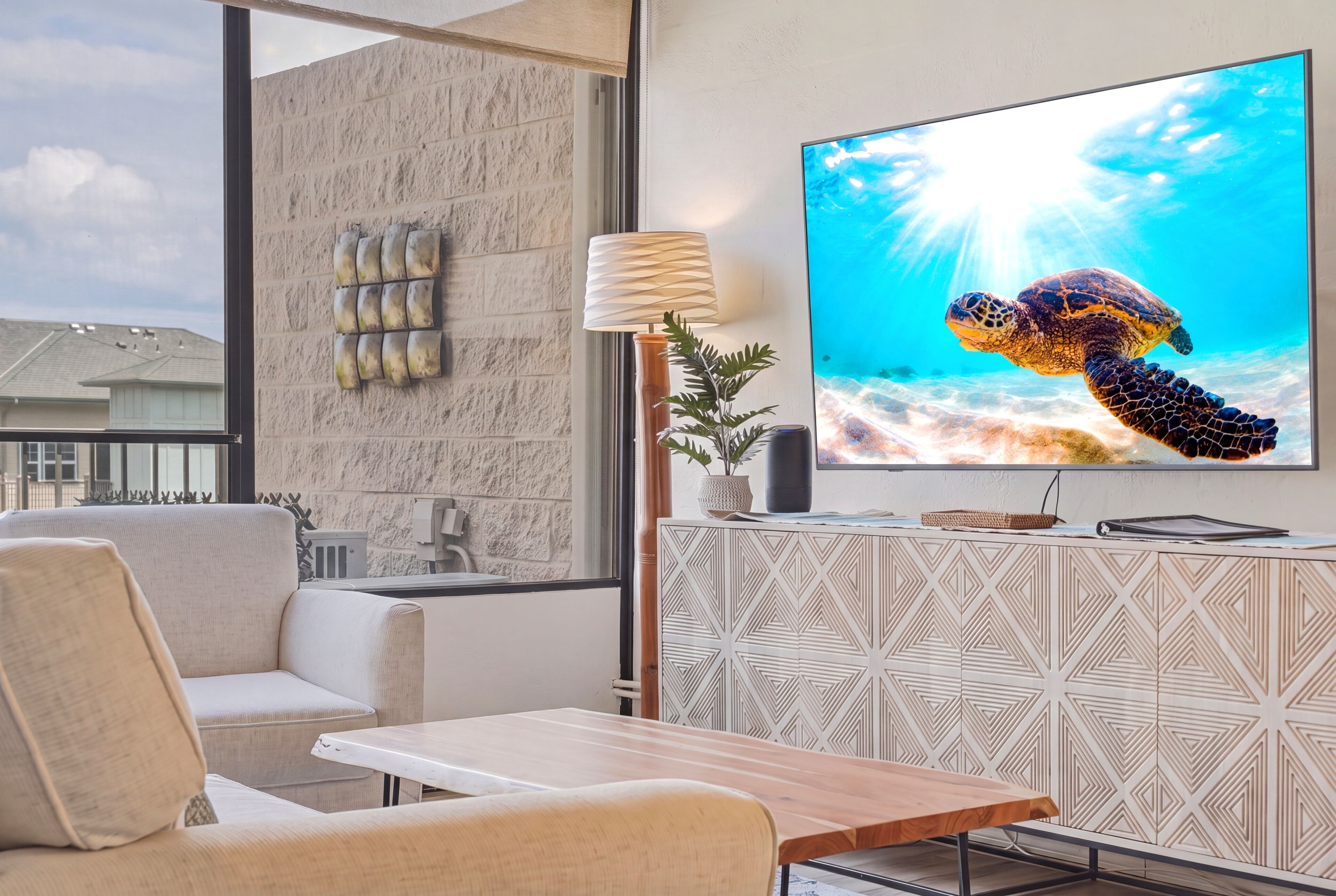 A modern living room with a large flat-screen TV displaying a sea turtle, a sofa, a coffee table, and a decorative wall panel.