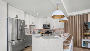 Une cuisine moderne avec des armoires blanches, des appareils en acier inoxydable, un îlot en marbre et un mur d’accent en bois.