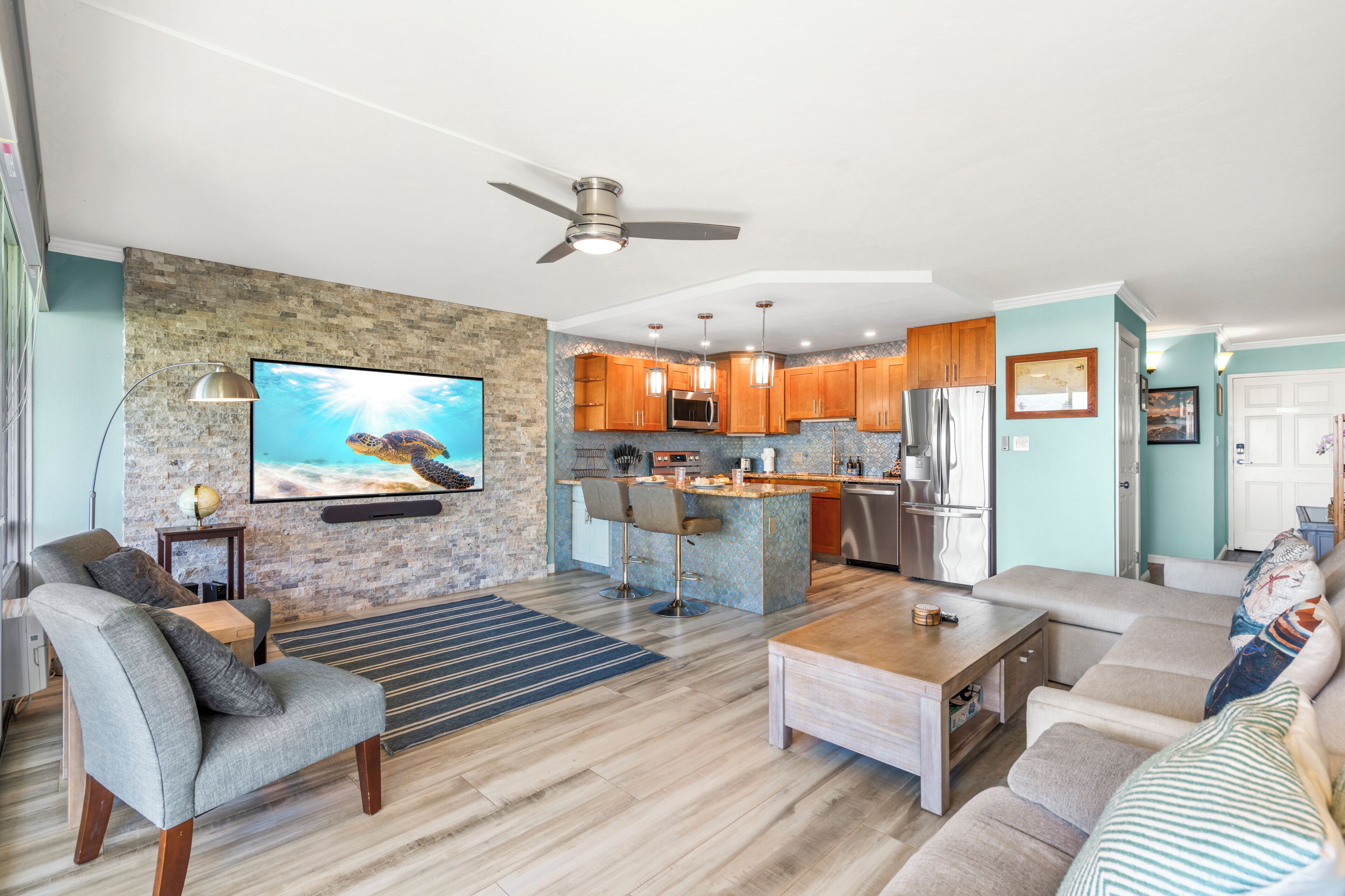 A modern living room with a TV, seating, a kitchen area, and a ceiling fan.