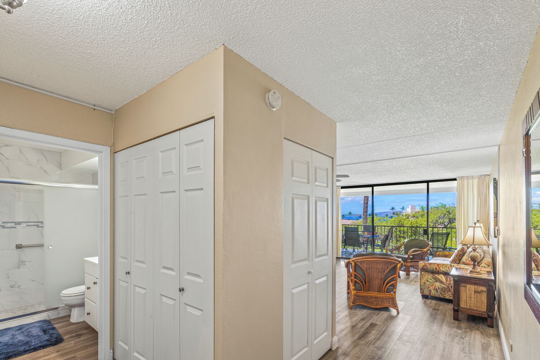 A spacious room with a large sliding glass door leading to a balcony with a view of the ocean. There is a seating area with wicker furniture and a small table.