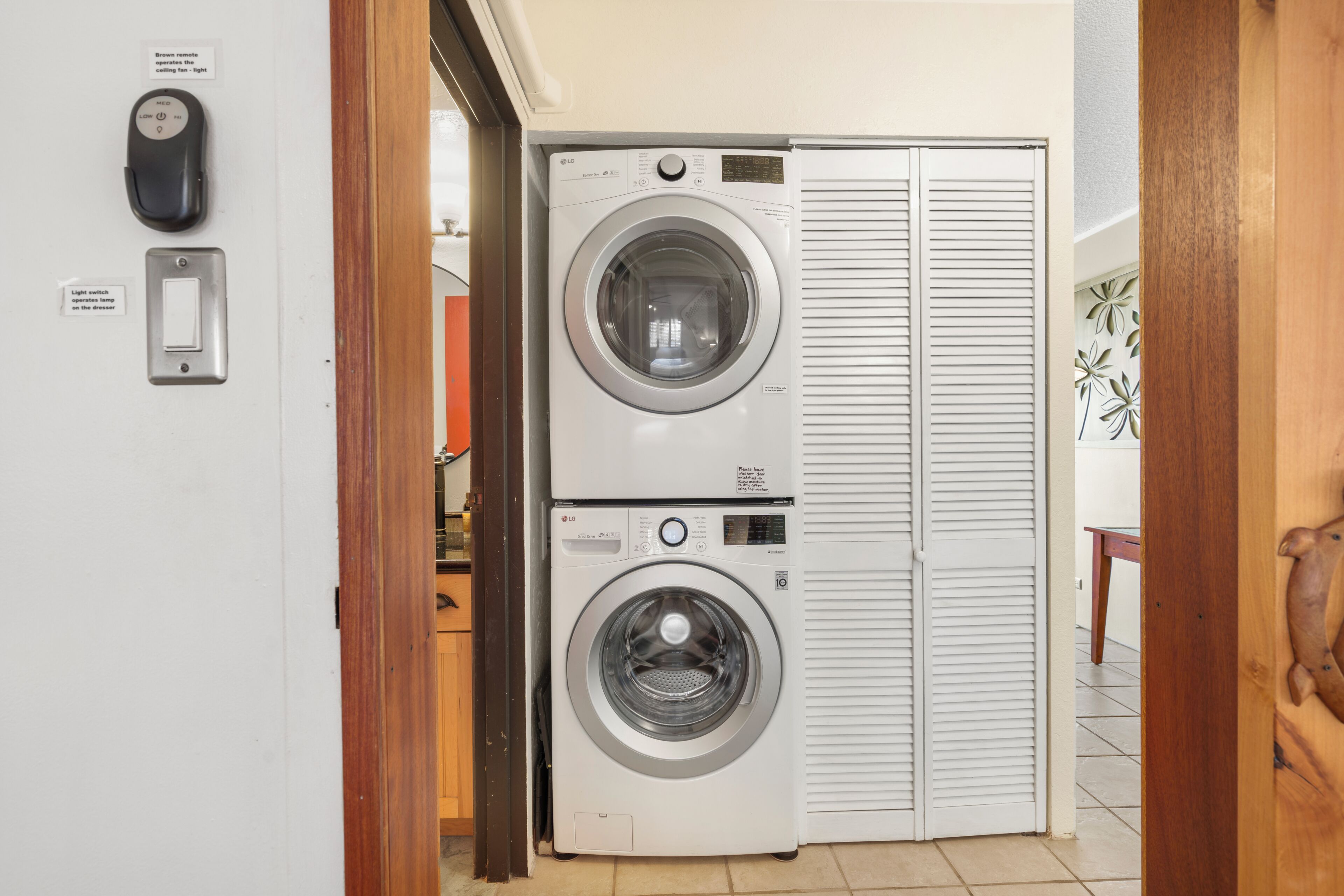 A laundry room with two stacked front-loading washing machines, a light switch, and a wall-mounted control panel.