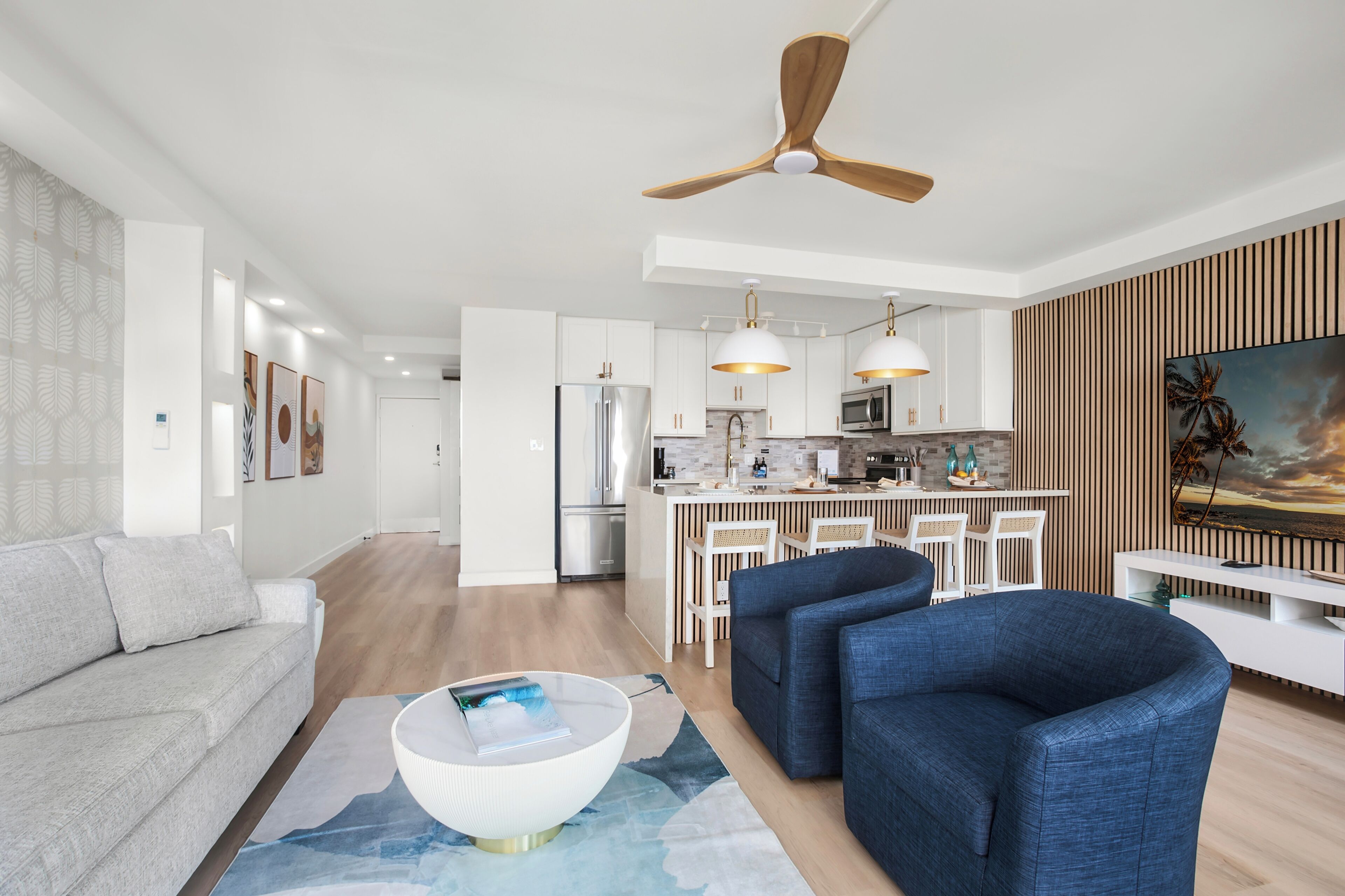 A modern living room with a sofa, two armchairs, a coffee table, and a dining area with a kitchen in the background.