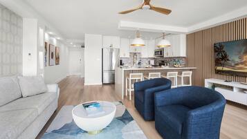 A modern living room with a sofa, two armchairs, a coffee table, and a dining area with a kitchen in the background.