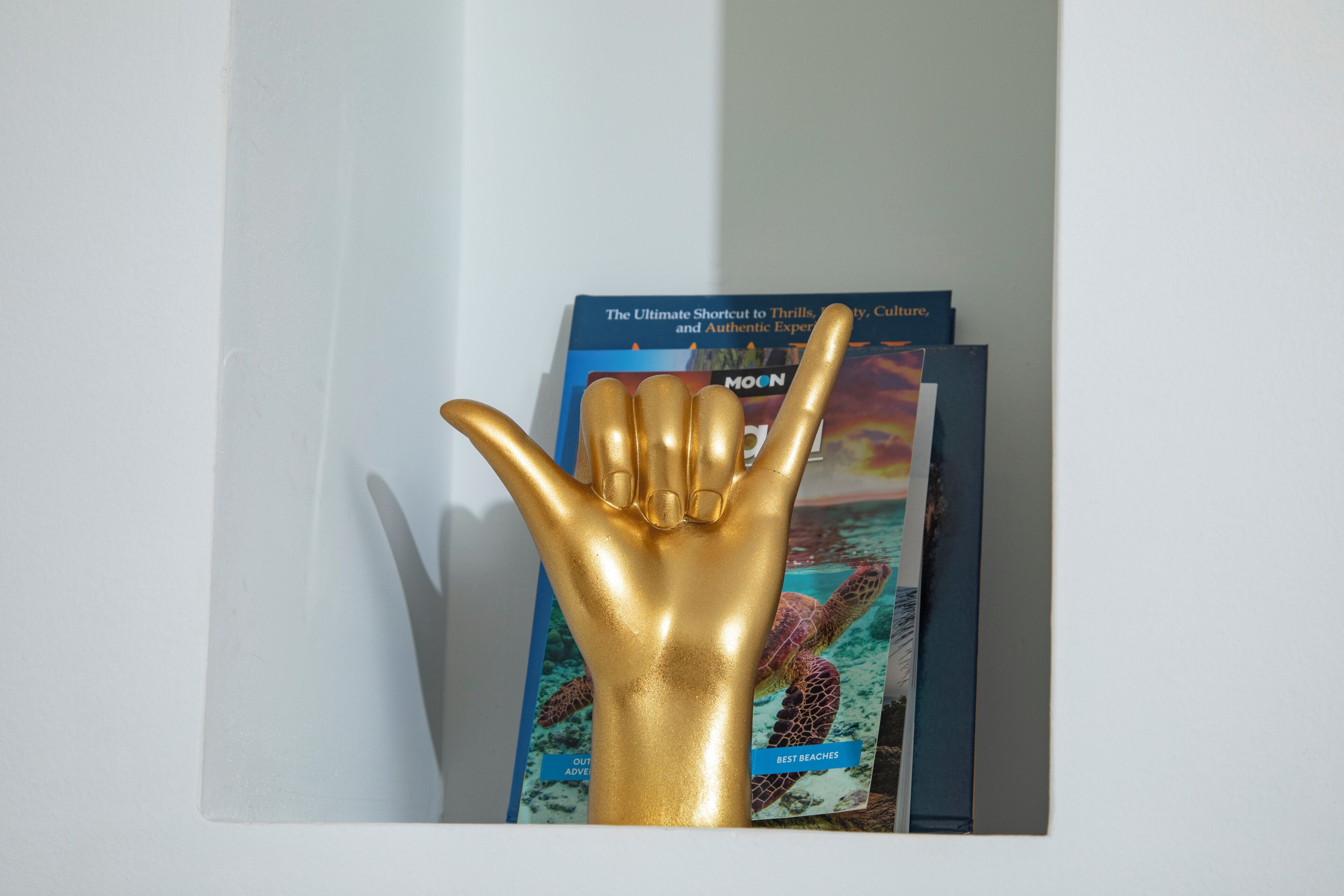 Una escultura dorada de una mano frente a una estantería con libros de viajes.