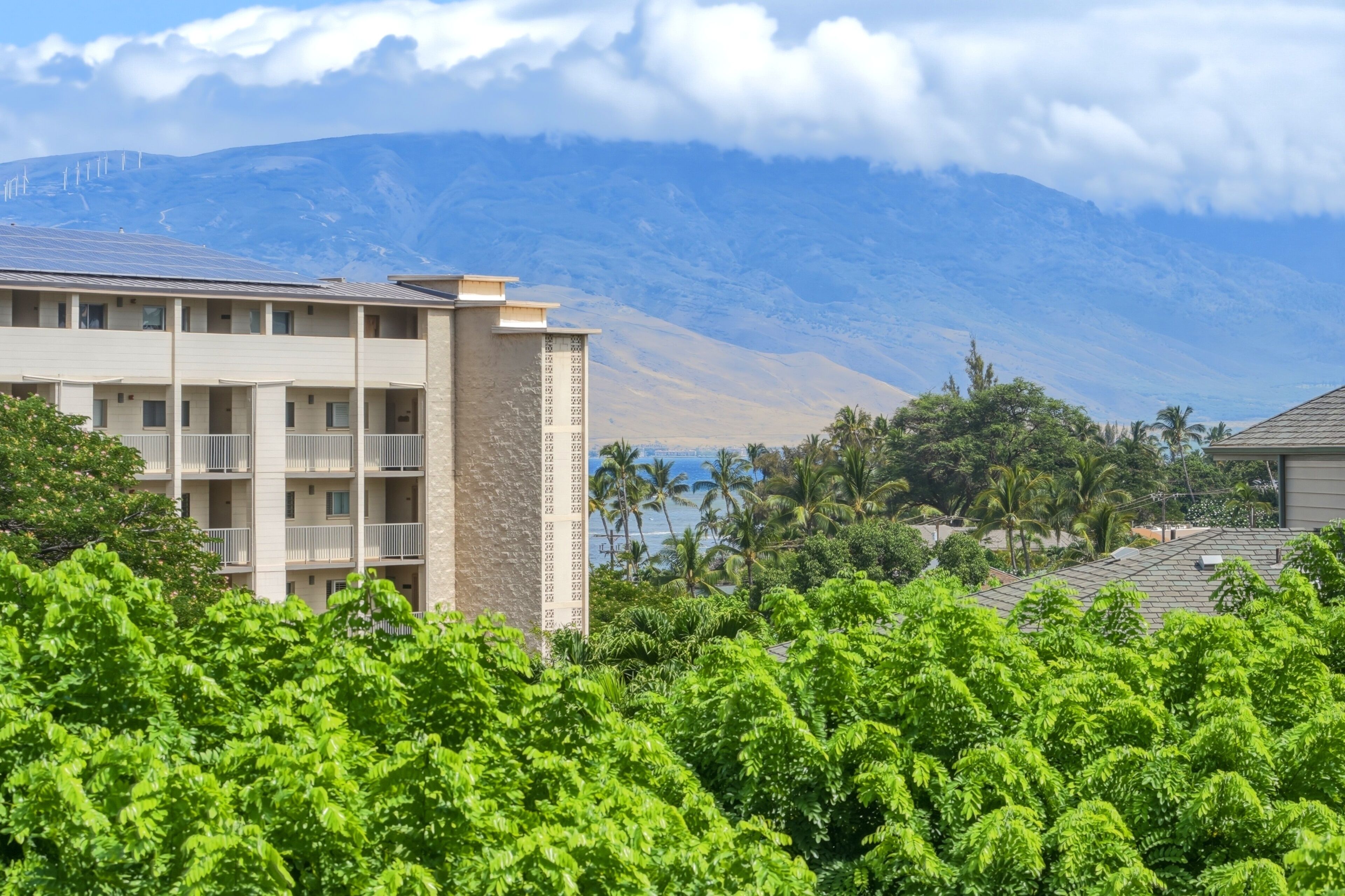 Un hotel de varios pisos con balcones, un telón de fondo montañoso y abundante vegetación en primer plano.
