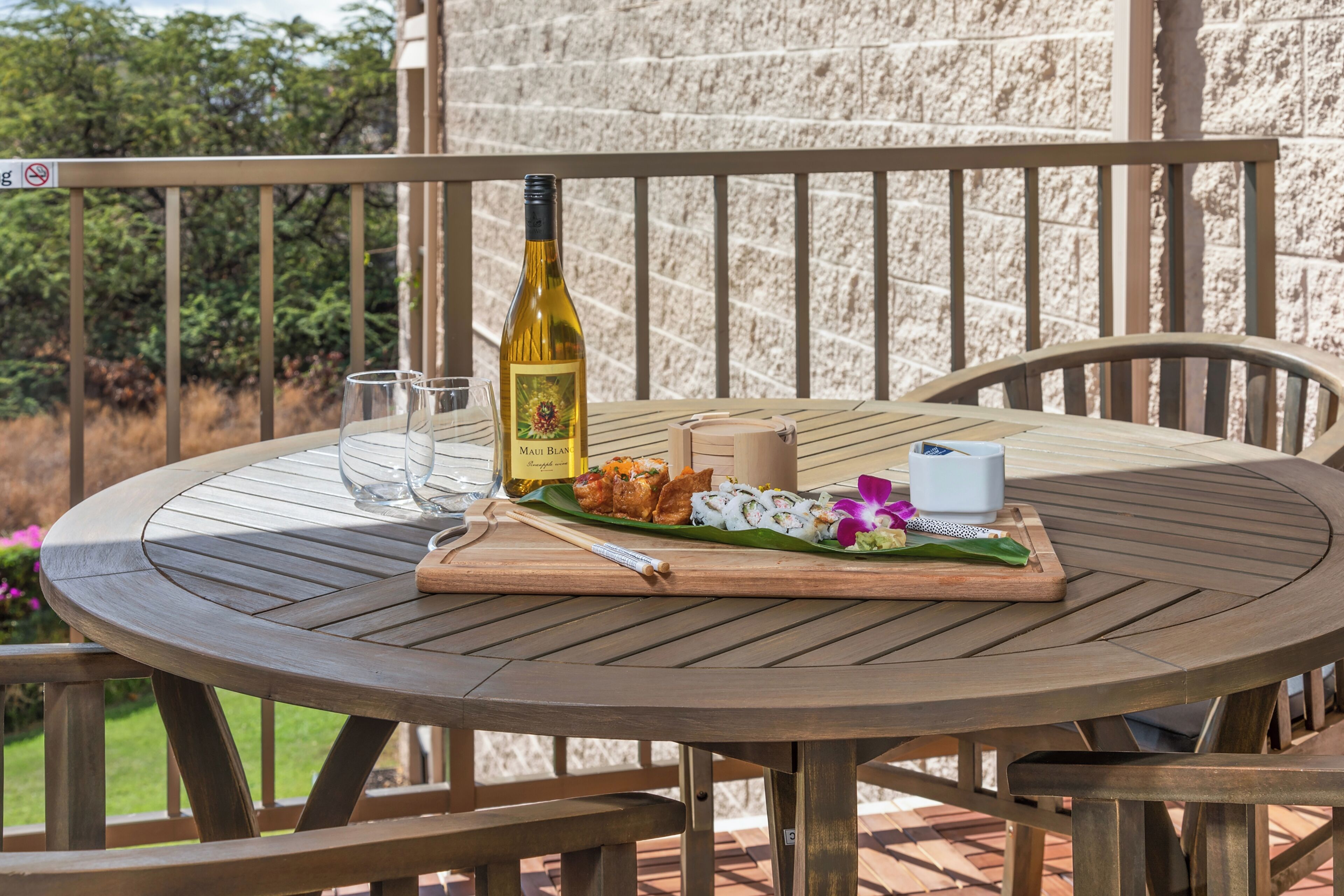 Une table ronde en bois, avec une bouteille de vin, un verre et une assiette de nourriture, sur un balcon.