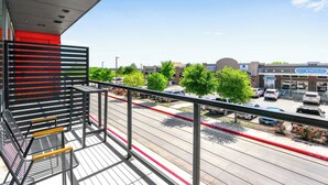 A balcony with metal railings overlooking a parking lot and a building with a sign that reads "ELECT DERMATOLOGY". - Pacific Island Inspired Stay | Amazing Location (New Braunfels)