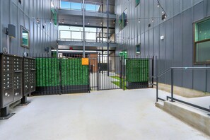 Entrada de un edificio moderno con un camino de entrada cerrado por una reja, taquillos metálicos y una escalera que conduce a un nivel superior.