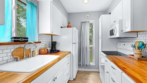 A modern kitchen with white cabinets, a wooden countertop, a sink, a refrigerator, a microwave, and a window with curtains. - Charming Lakeside Condo - Moments to Lake Fun (Canyon Lake)