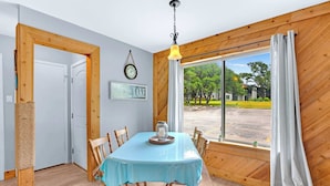 A dining area with a table set for six, wooden walls, a large window with curtains, a clock, and a sign that reads "LAKE". - Charming Lakeside Condo - Moments to Lake Fun (Canyon Lake)