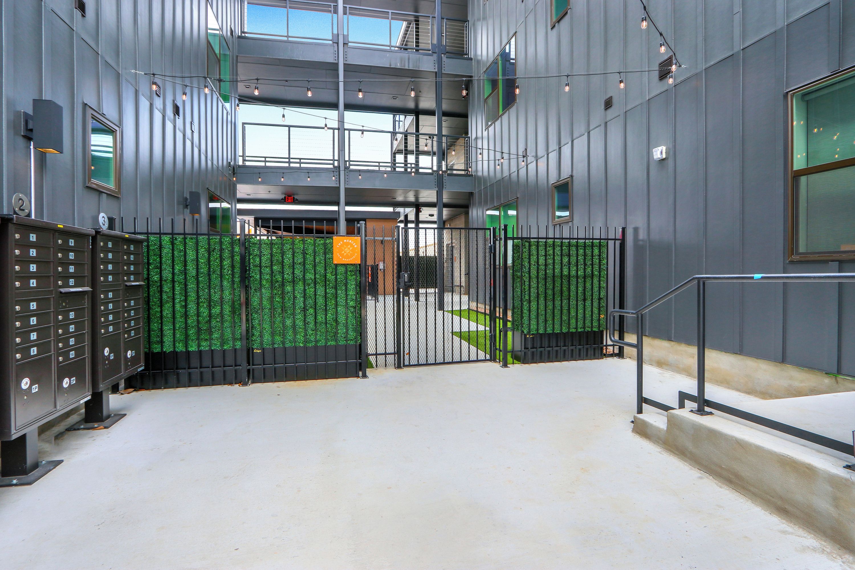 A modern building entrance with a gated driveway, metal lockers, and a staircase leading to an upper level.