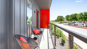 A balcony with two wicker chairs, a small table, and a red door. - Pure Texas Poolside Oasis | Steps to Entertainment (New Braunfels)