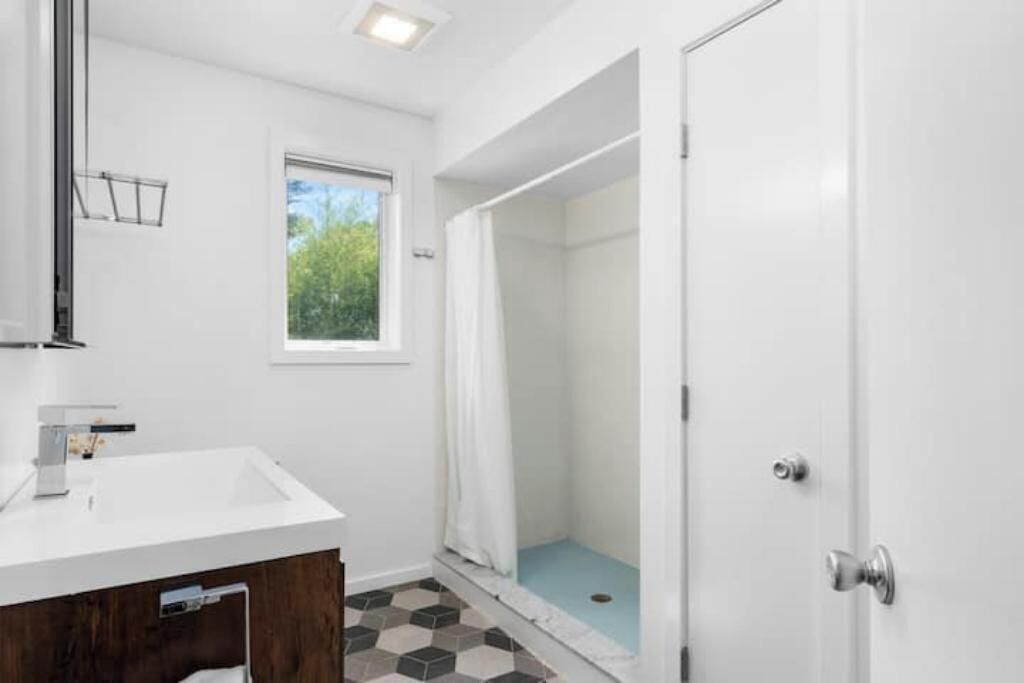 Un baño con un lavabo blanco, ducha y ventana.