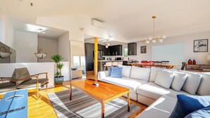 Una sala de estar moderna con una mesa de centro de madera, un sofá blanco y una zona de comedor con un pilar amarillo.